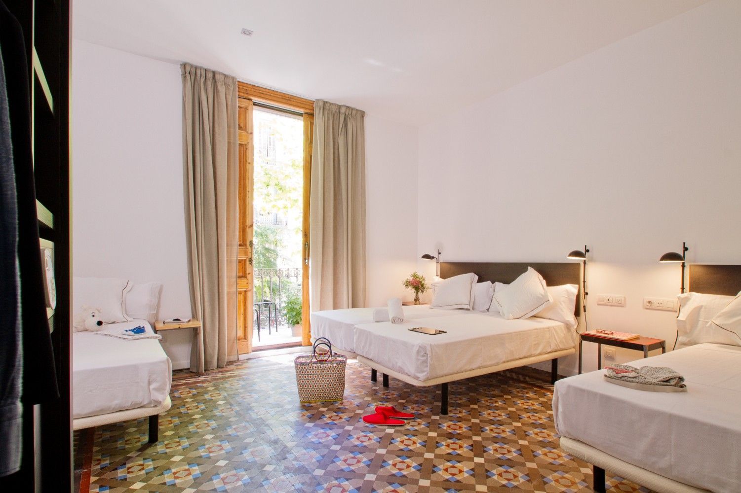 Una habitación de hotel bien iluminada con tres camas blancas, pisos de baldosas estampadas.