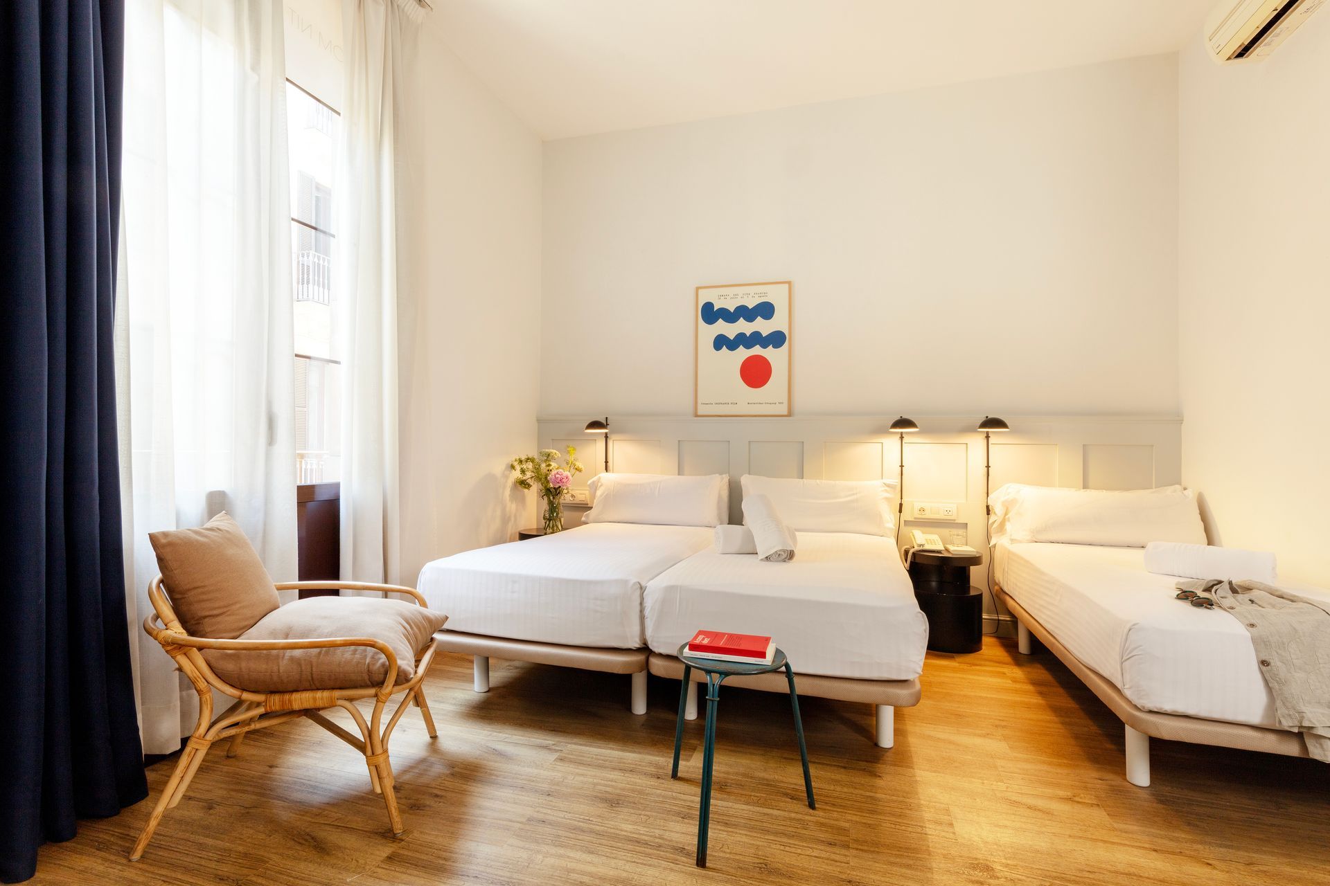 Habitación luminosa con dos camas individuales, silla de mimbre y cortinas que van del suelo al techo.