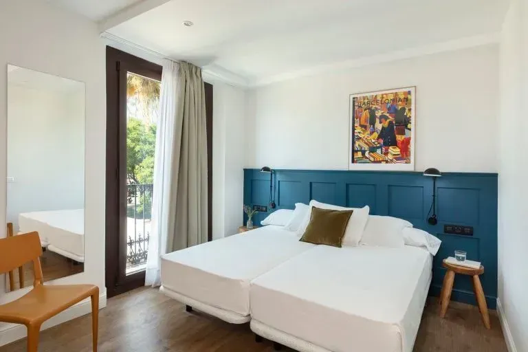 Un dormitorio con dos camas individuales blancas, una cabecera de madera azul, una silla de madera.
