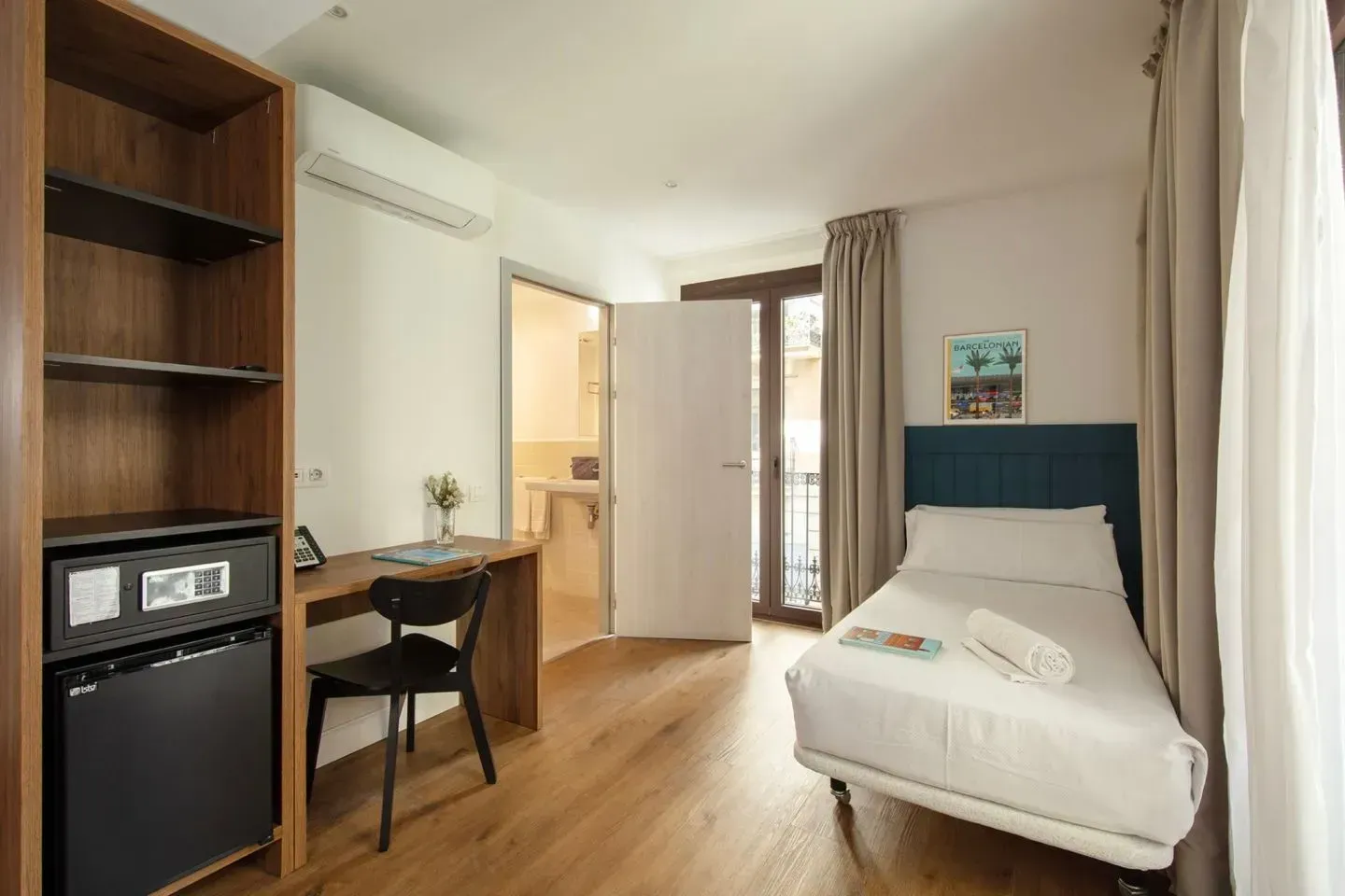Una habitación de hotel con una cama doble, un escritorio de madera con una silla negra, un mueble de almacenaje abierto.