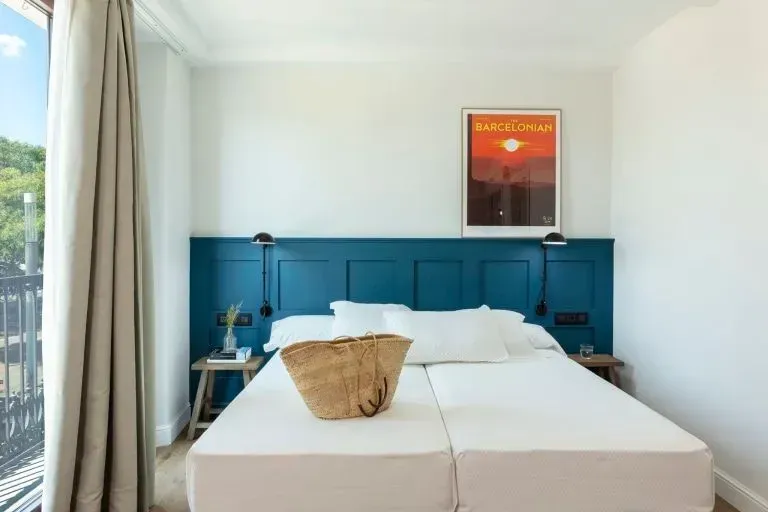 Un dormitorio de hotel luminoso cuenta con una cama grande con cabecera con paneles de color verde azulado.