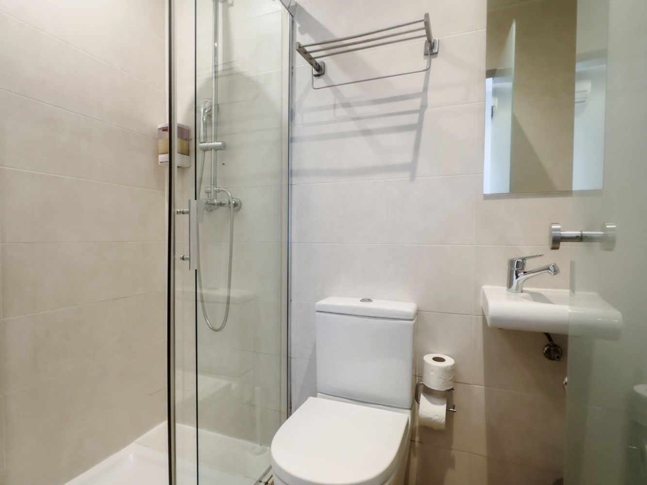 Un baño moderno de color beige con cabina de ducha de cristal, un inodoro blanco, un toallero montado en la pared.
