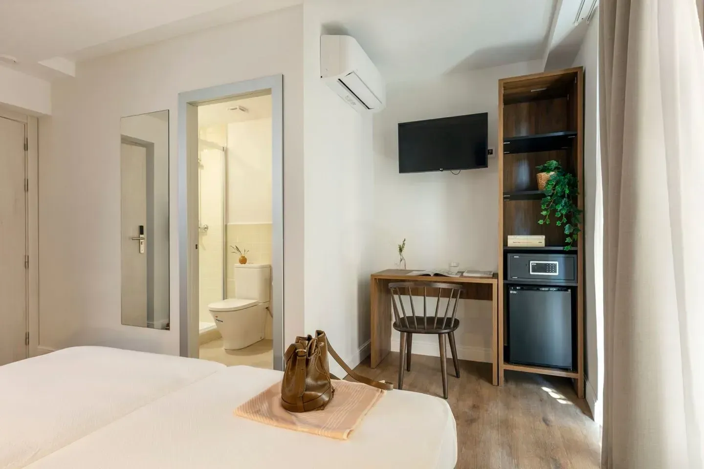 Un dormitorio de hotel con una cama en primer plano, una puerta abierta a un baño.