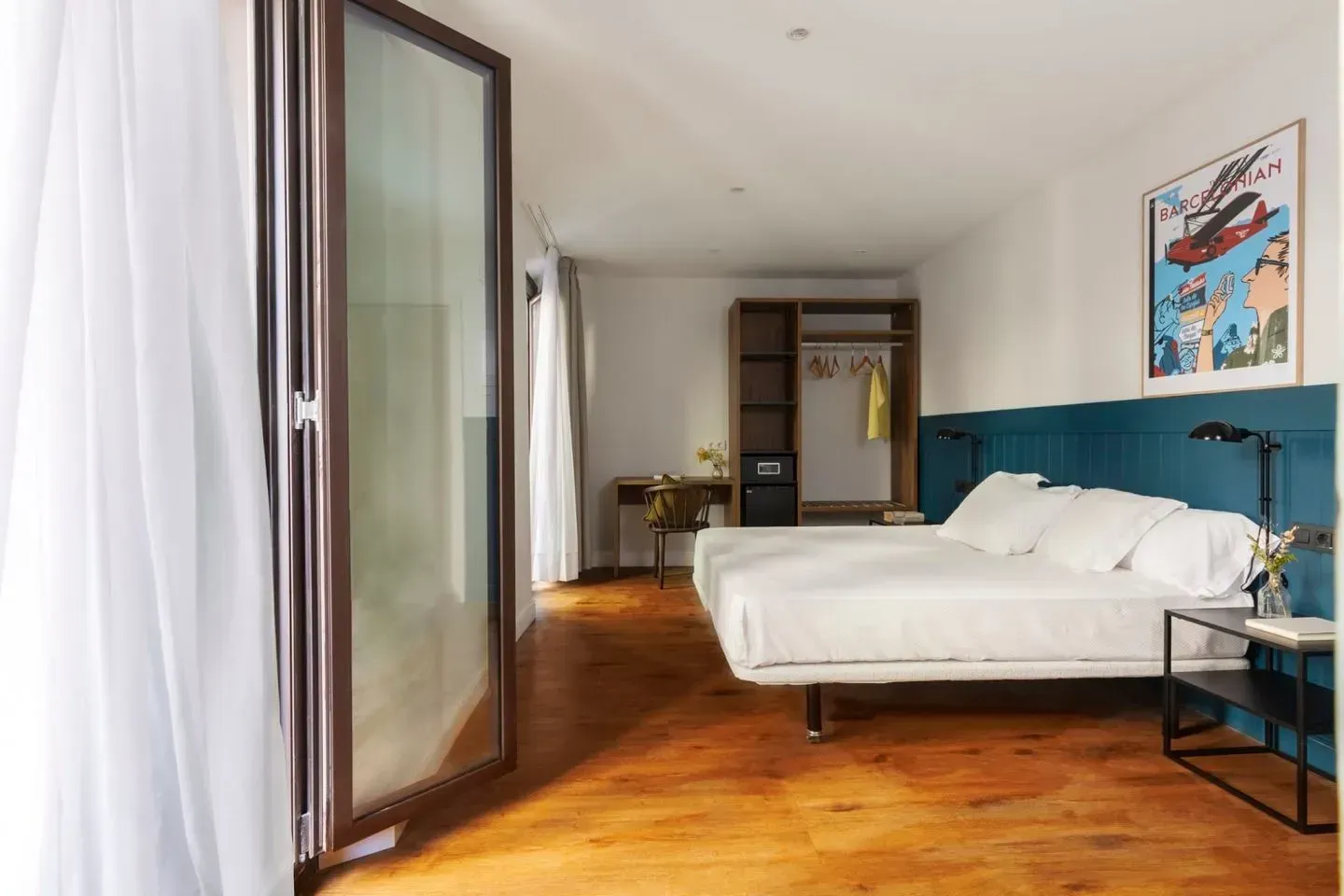 Un dormitorio moderno con ropa de cama blanca, suelos de madera, cabecero azul, un armario.