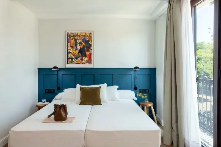 Un dormitorio luminoso con una cama blanca, un cabecero con paneles de color azul oscuro, lámparas de noche minimalistas.