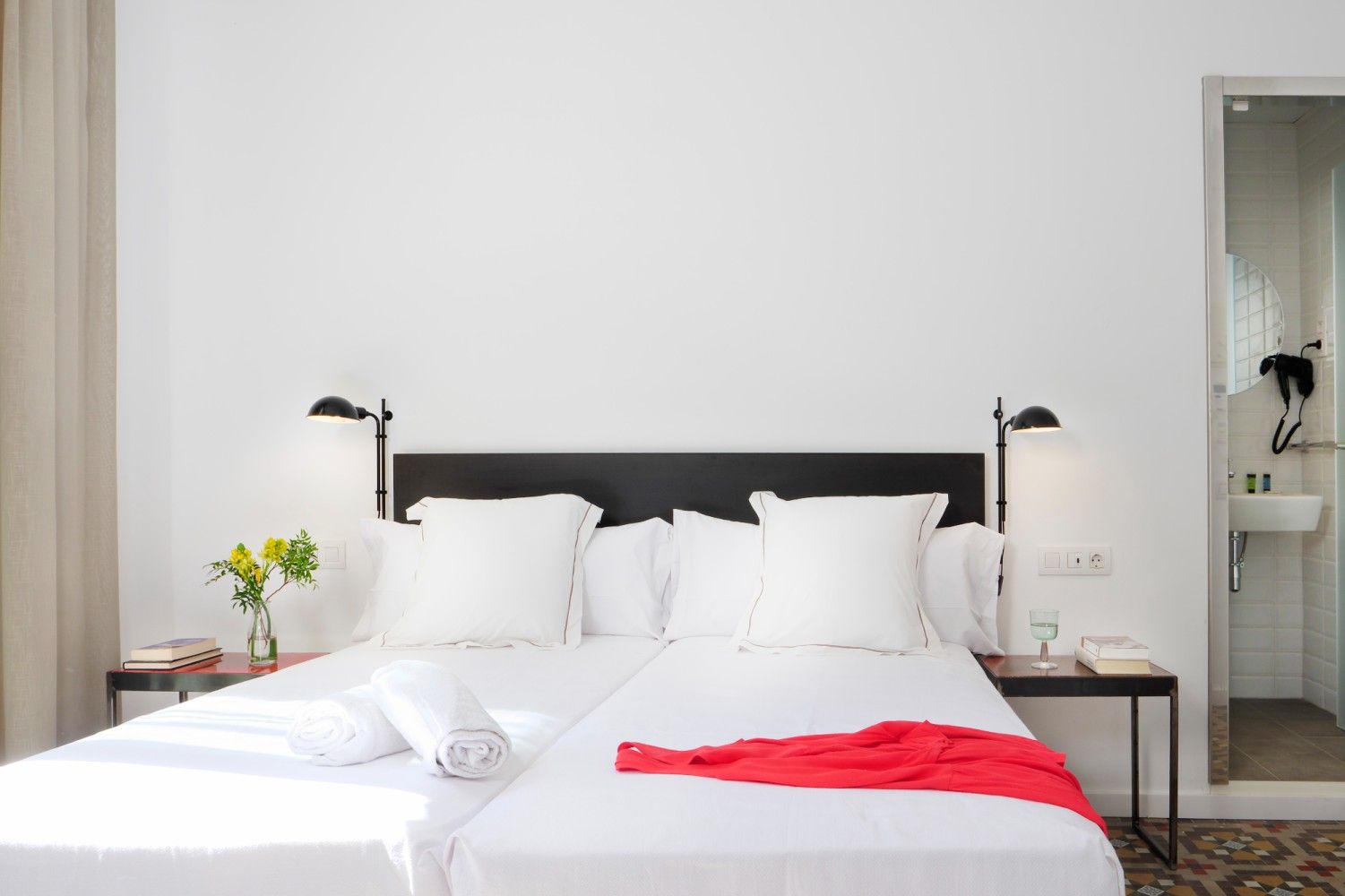 Una habitación de hotel con dos camas unidas, sábanas blancas, cabecero negro, lámparas de pared.