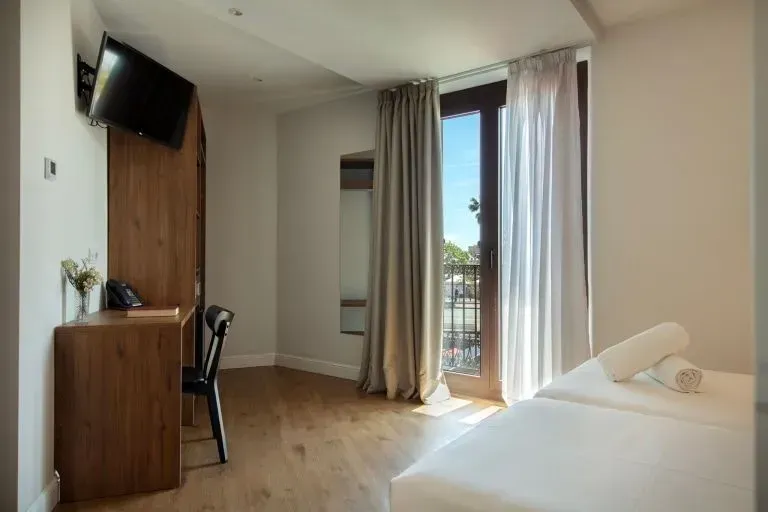 Una habitación de hotel con suelo de madera, un escritorio y una silla de madera, un televisor montado en la pared.