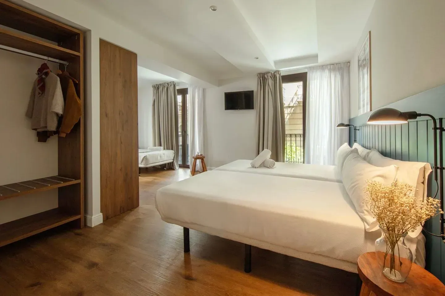 Una moderna habitación de hotel con dos camas individuales blancas, suelo de madera, un armario abierto.