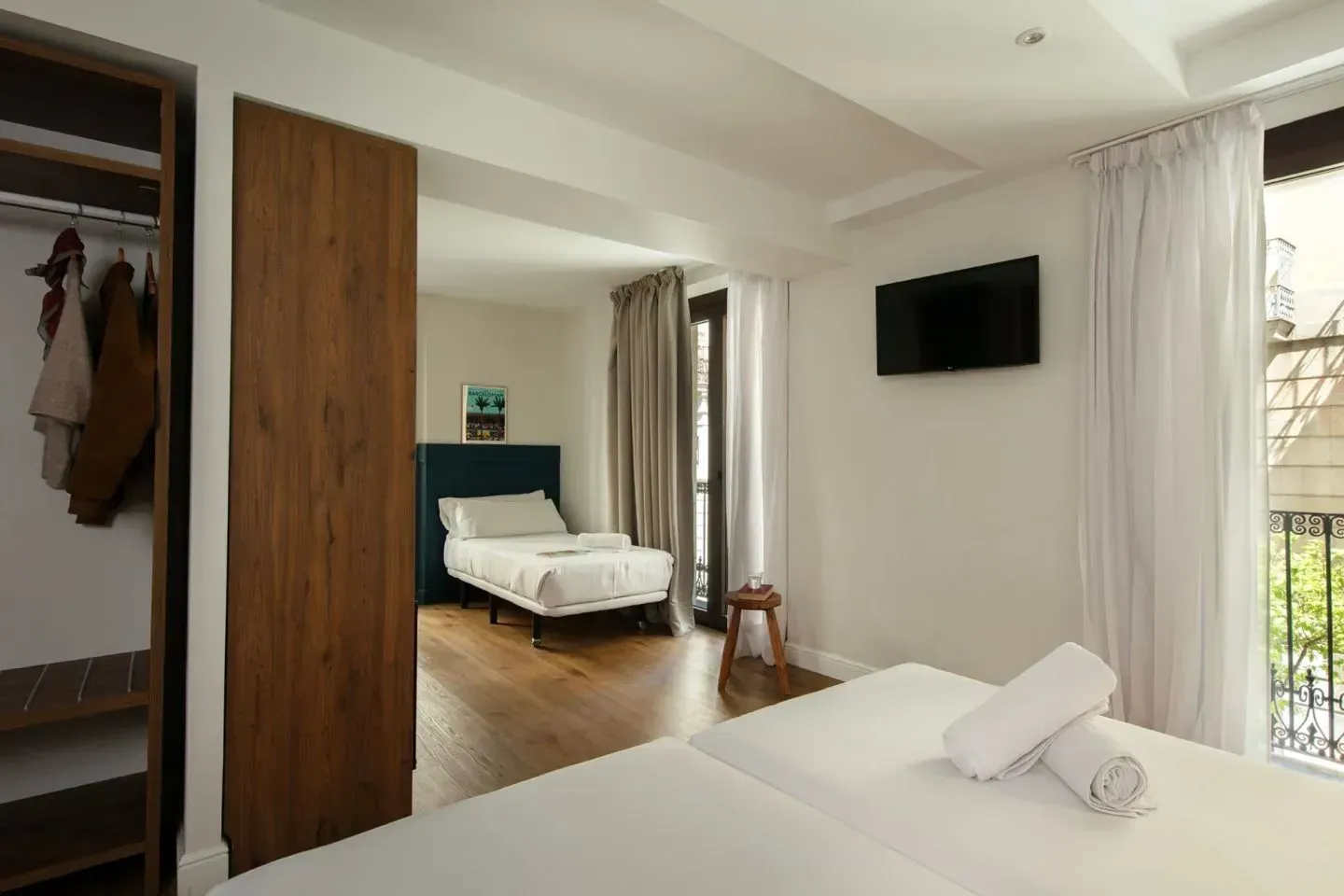 Una luminosa habitación de hotel con dos camas blancas, un armario de madera, un televisor montado en la pared .