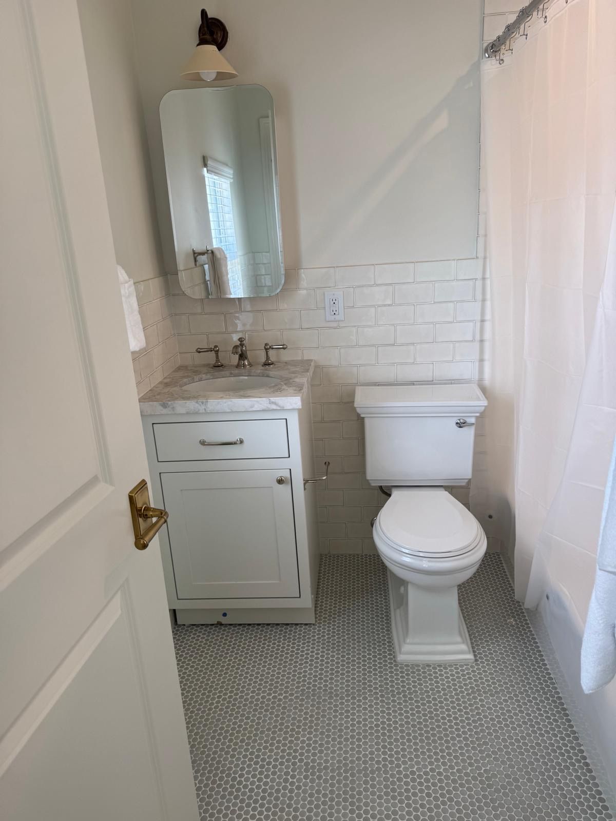 Small white bathroom with a toilet, sink, and shower; gray floor tiles.
