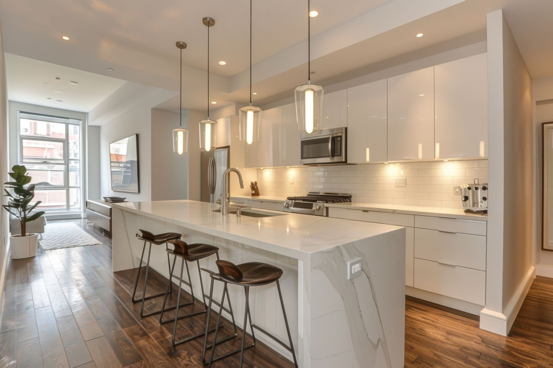 Modern white kitchen with island, stools, pendant lights, hardwood floors.