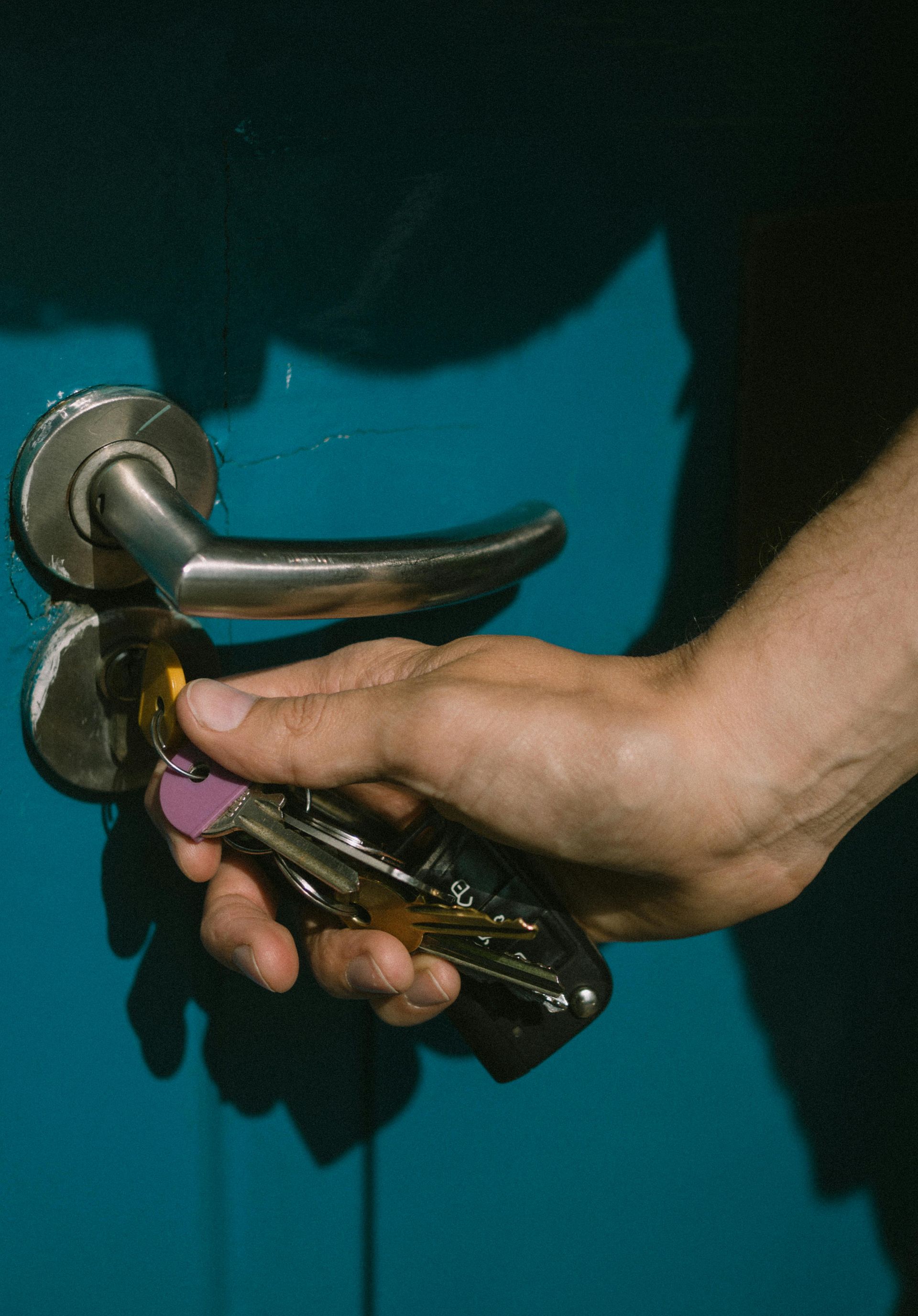 Hand with keys unlocking a door. Blue door, silver handle and lock.