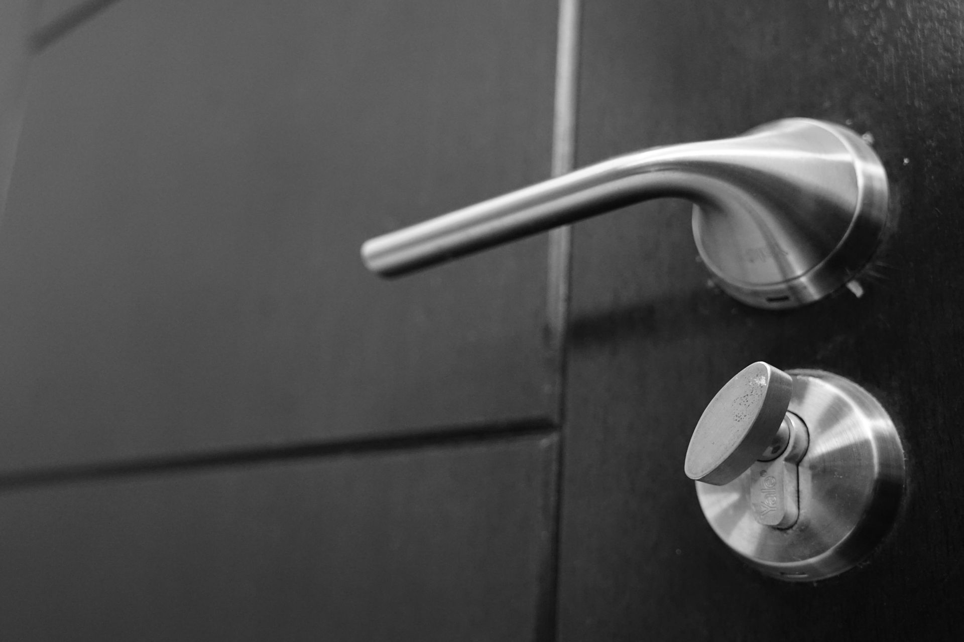 Black and white close-up of a door handle and lock on a dark door.
