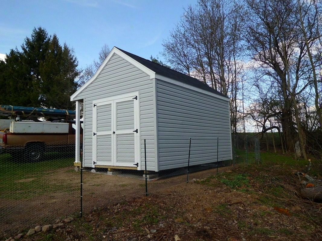 Gray shed with white doors, black roof, in a grassy backyard, blue sky in the background.