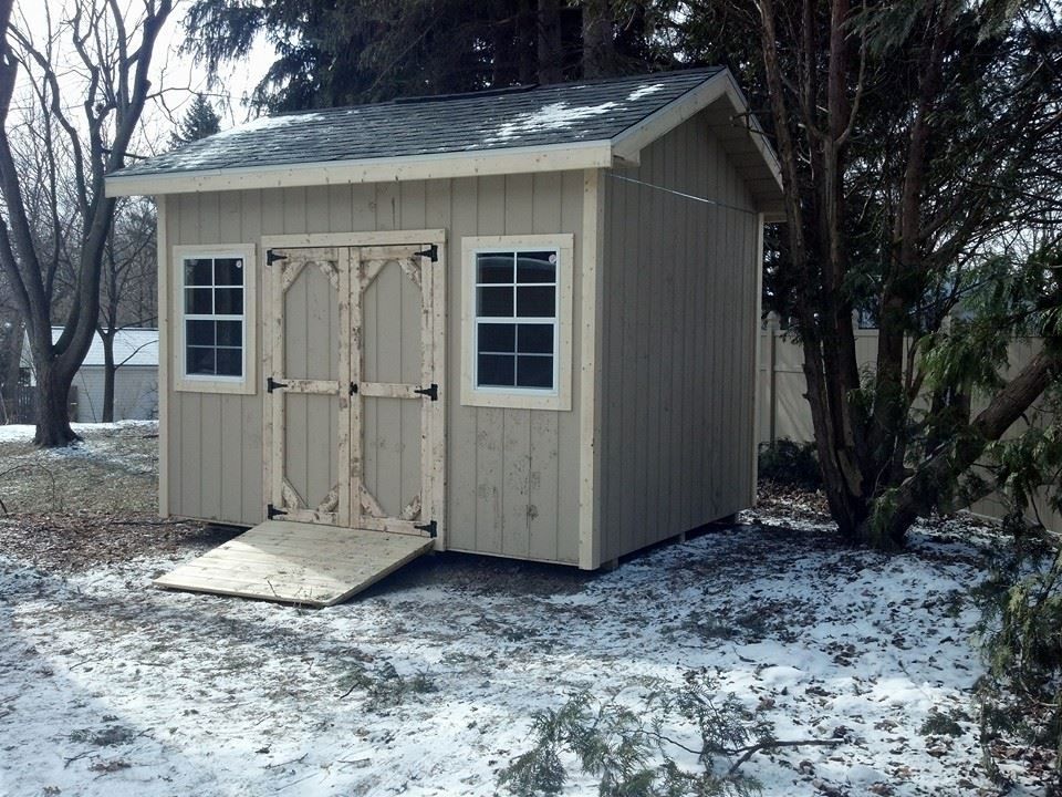 Beige wooden shed with ramp, two windows, and double doors; snow on ground.