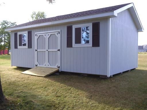 Light blue shed with brown shutters and double doors, small ramp, on grass.