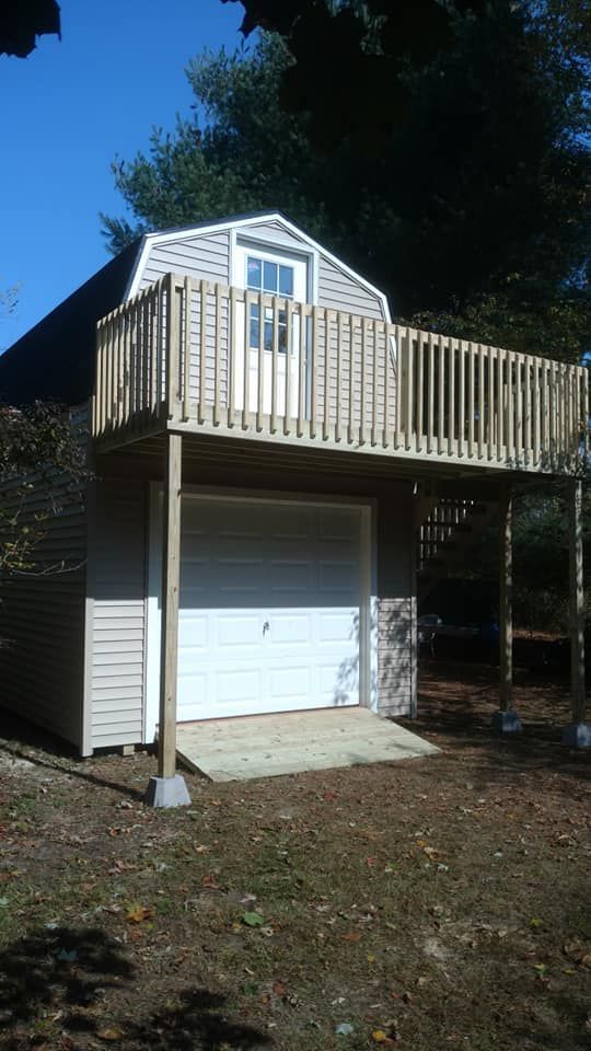 Two-story tan shed with a deck on top. A white garage door is visible.