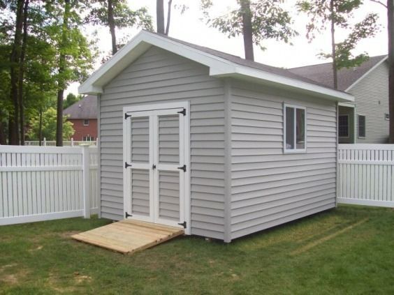 Gray shed with double doors, small window, and ramp, in a yard with a white picket fence.
