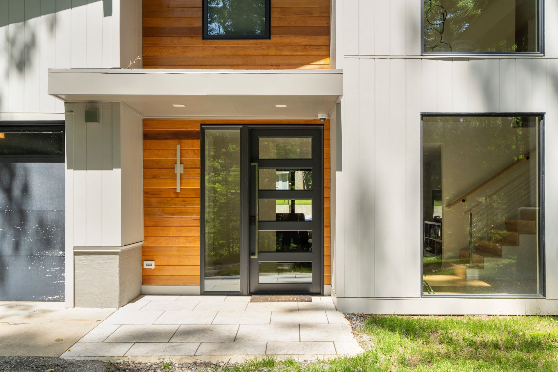 Modern house entrance with wood paneling, glass door, and large windows.