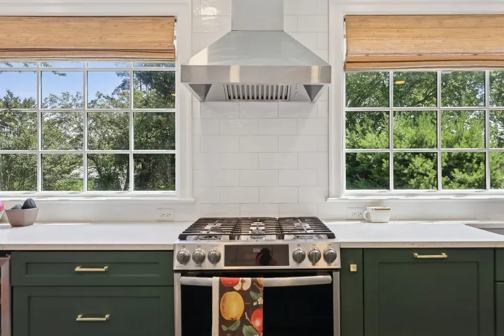 A kitchen with green cabinets , a stove , and a window.