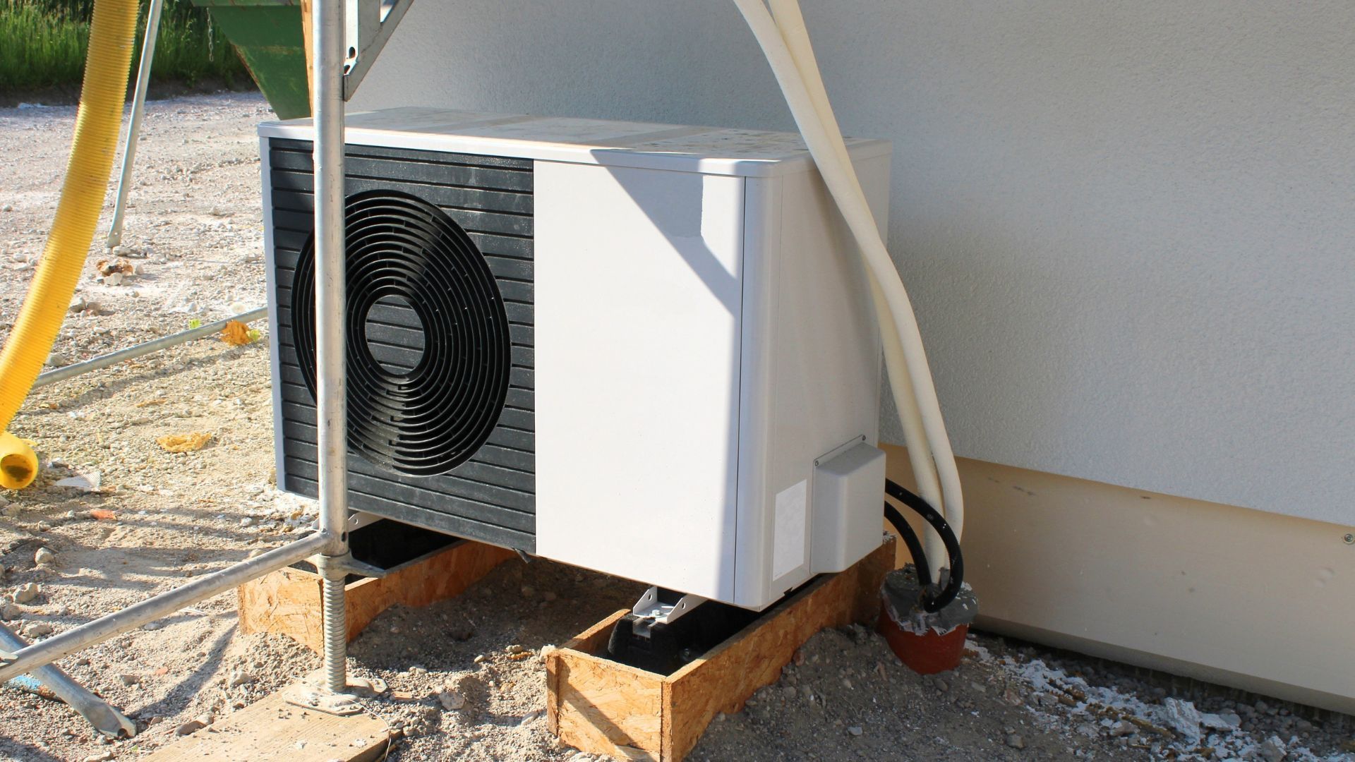 White air conditioning unit on a wooden base, mounted on a wall outside.