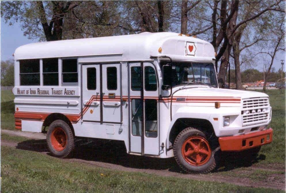 White and orange school bus parked on grass with trees in the background