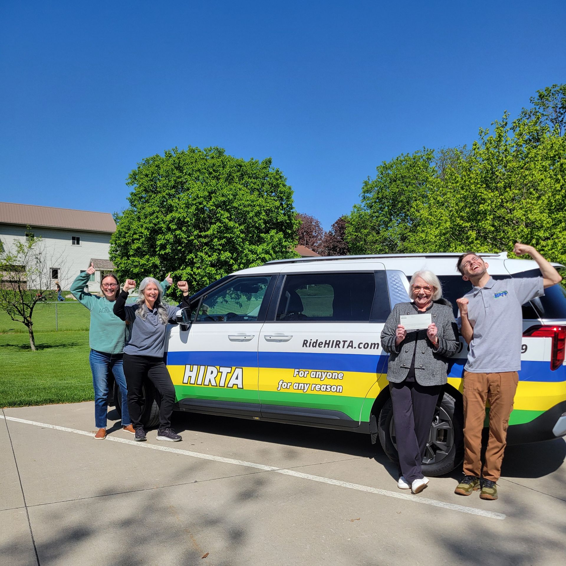 People posing beside a white van with green and yellow stripes on a sunny suburban street