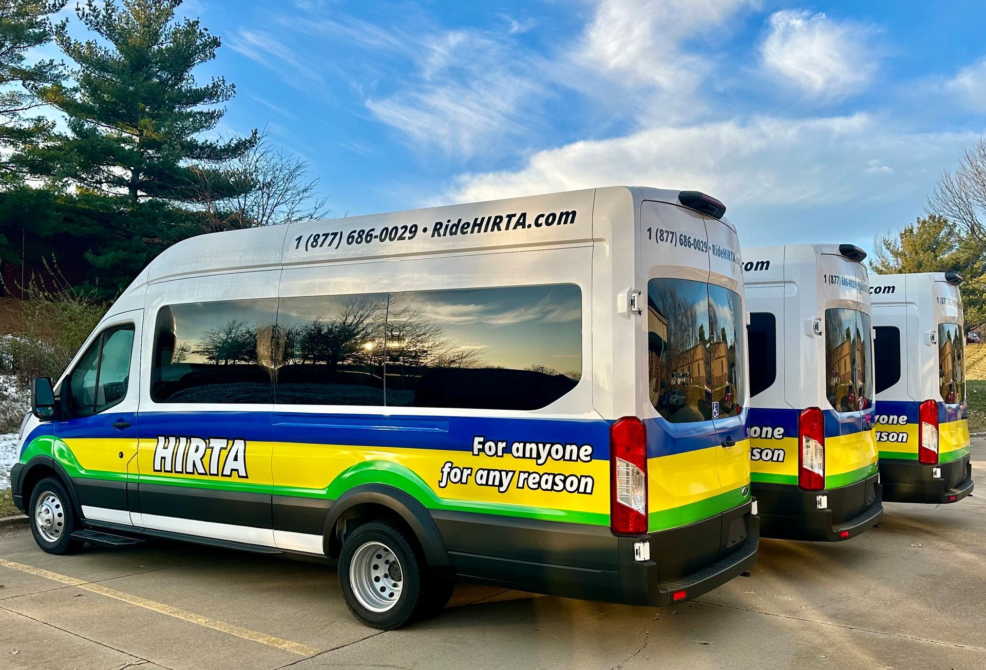 Shuttle vans in green, yellow and blue parked in a row under a blue sky.