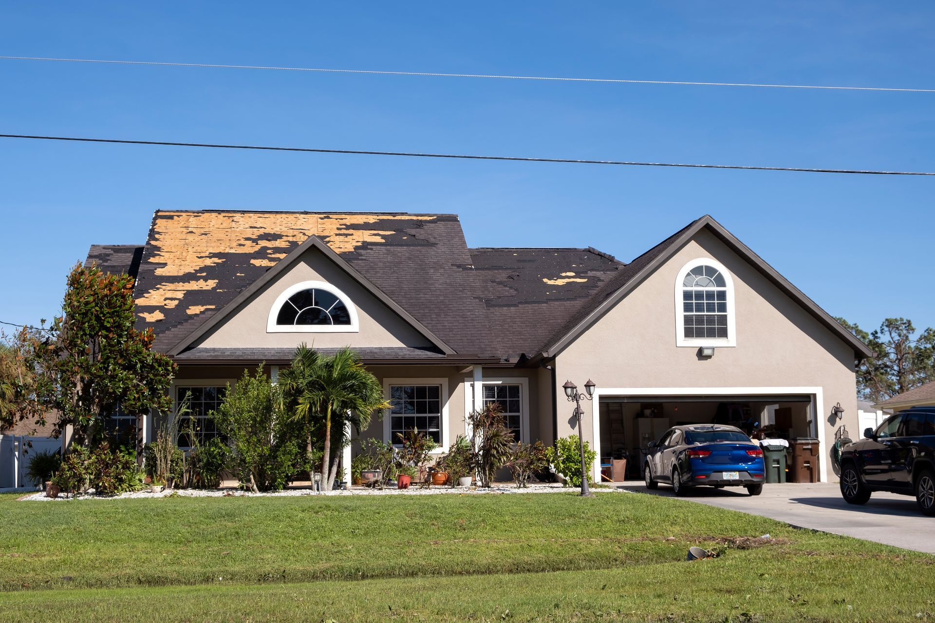 Single-story suburban house with beige siding, dark roof, and two cars parked in the driveway