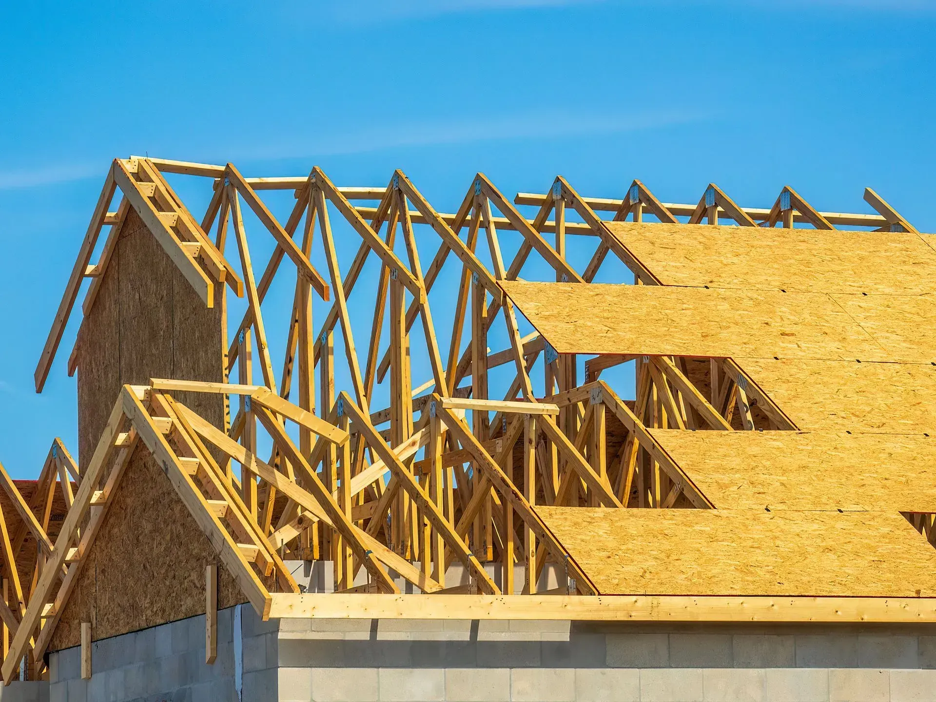 Partially framed house with wooden trusses and OSB sheathing under a blue sky