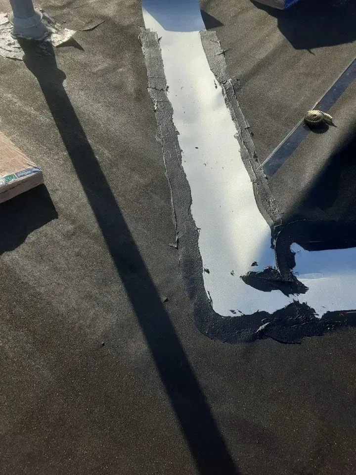 White roof sealant patch on a dark flat roof, with a person’s shadow and a small object nearby