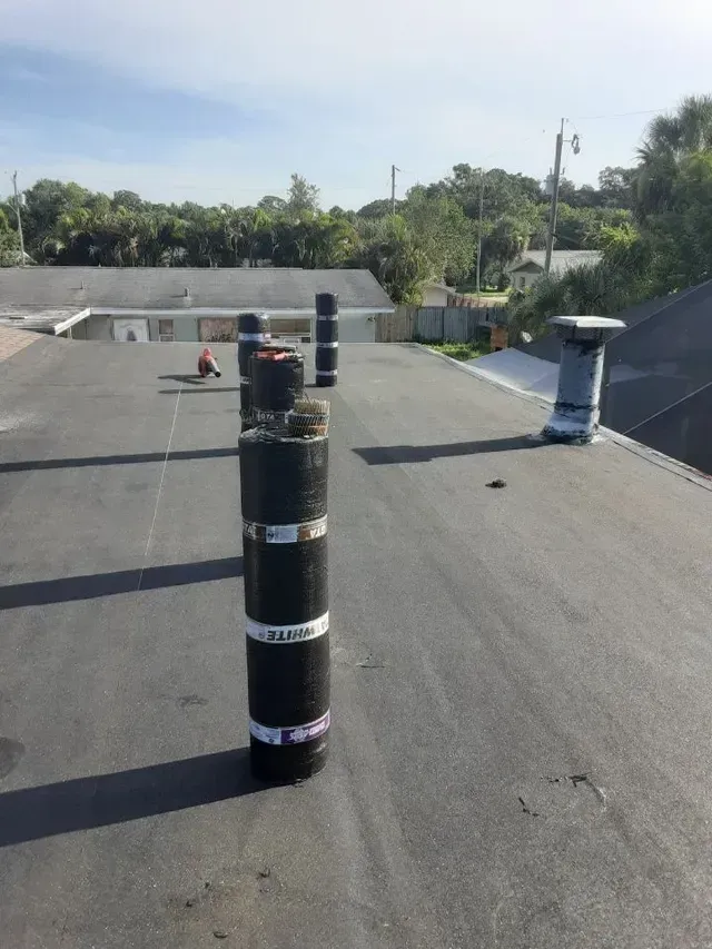 Black rooftop vent pipes on a flat roof under a clear sky.