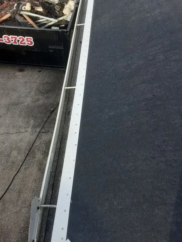 Rooftop edge with white trim beside a dark roof and an adjacent construction dumpster.