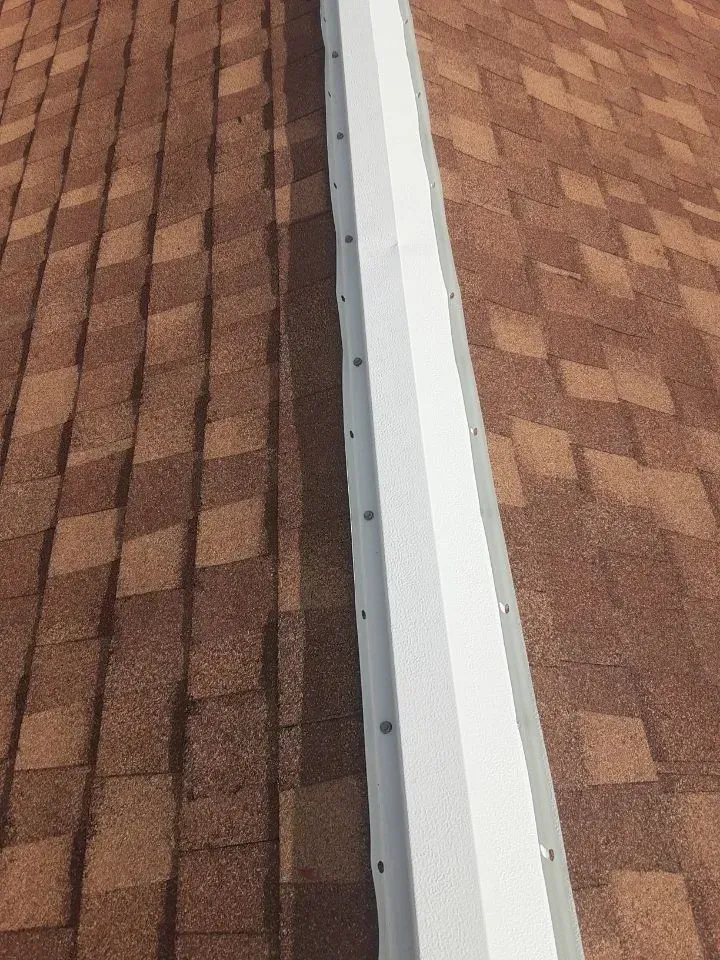 Close-up of a roof seam with white flashing between two brown shingle sections.