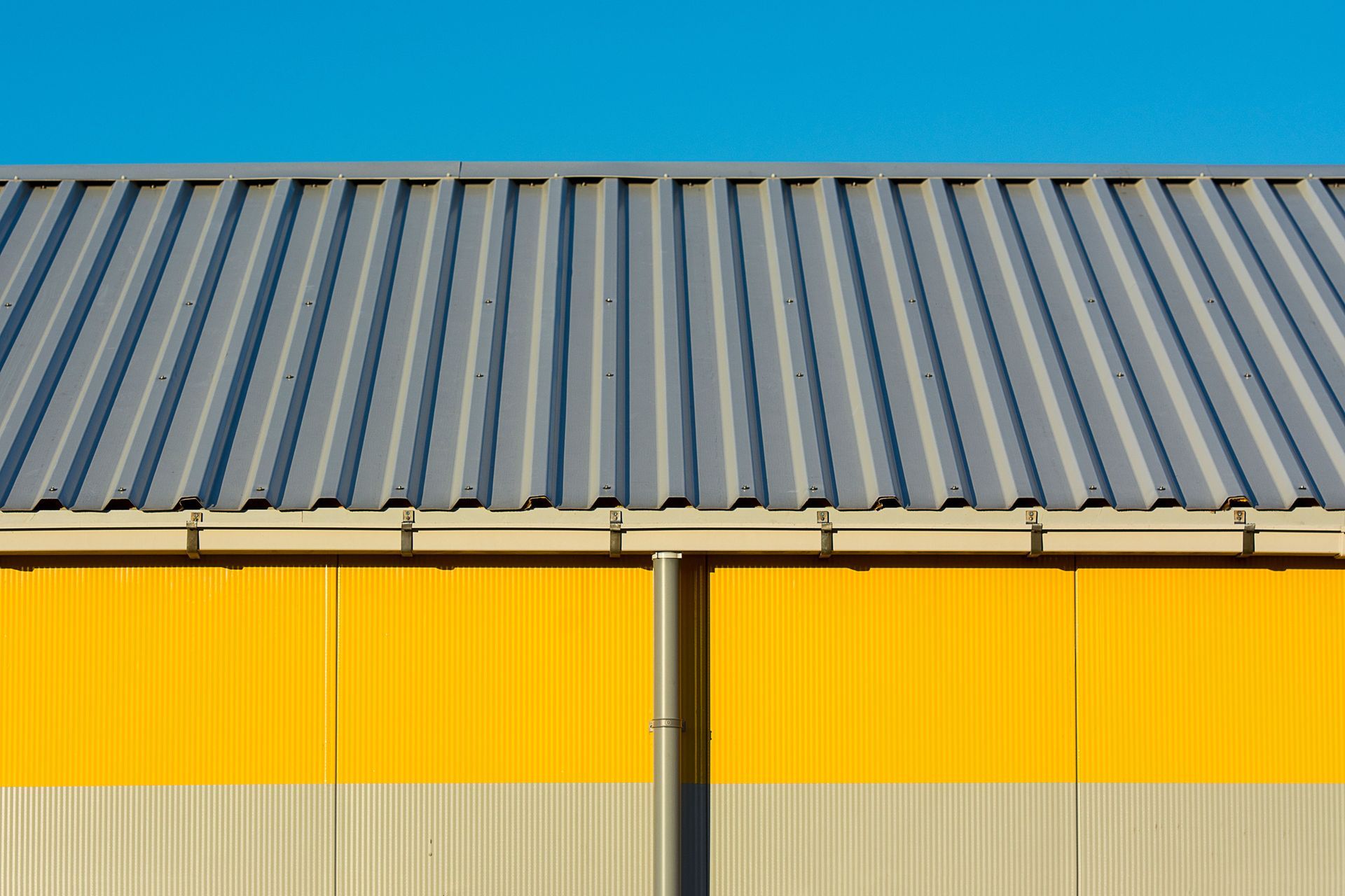 Yellow and gray corrugated metal building wall with a blue roof against a clear sky