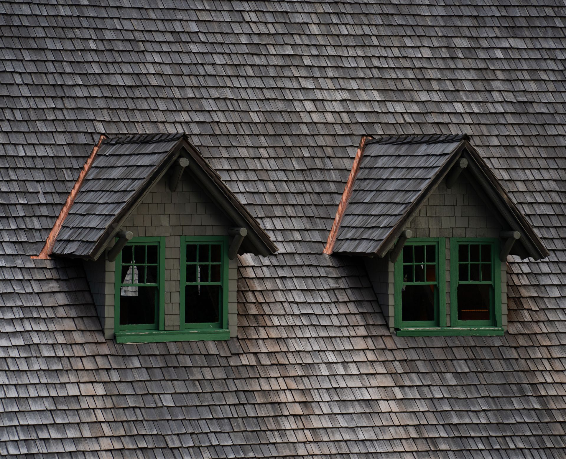 Two green-trimmed dormer windows on a gray shingled roof