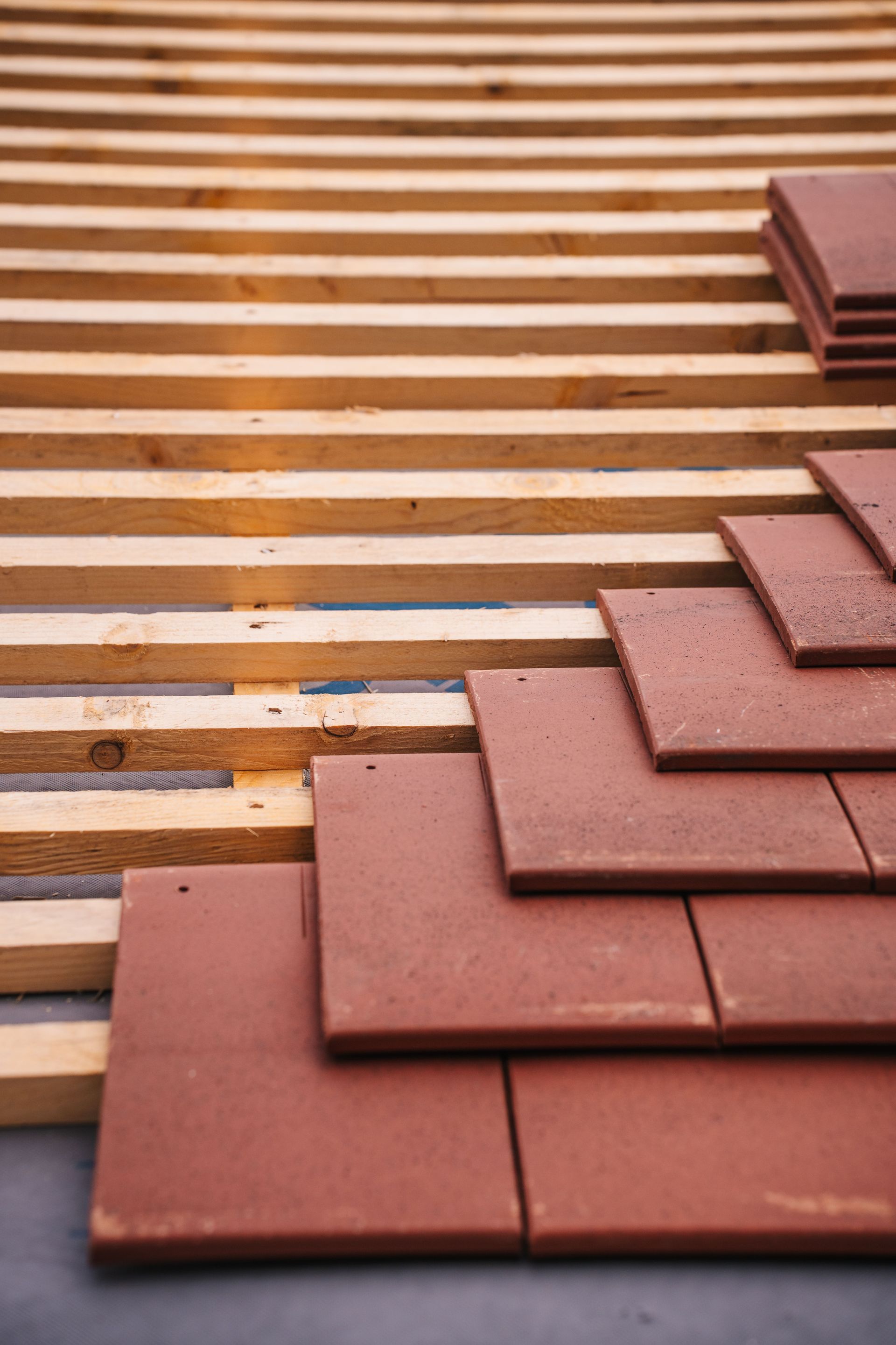 Brown roof tiles being installed over wooden slats on a roof frame