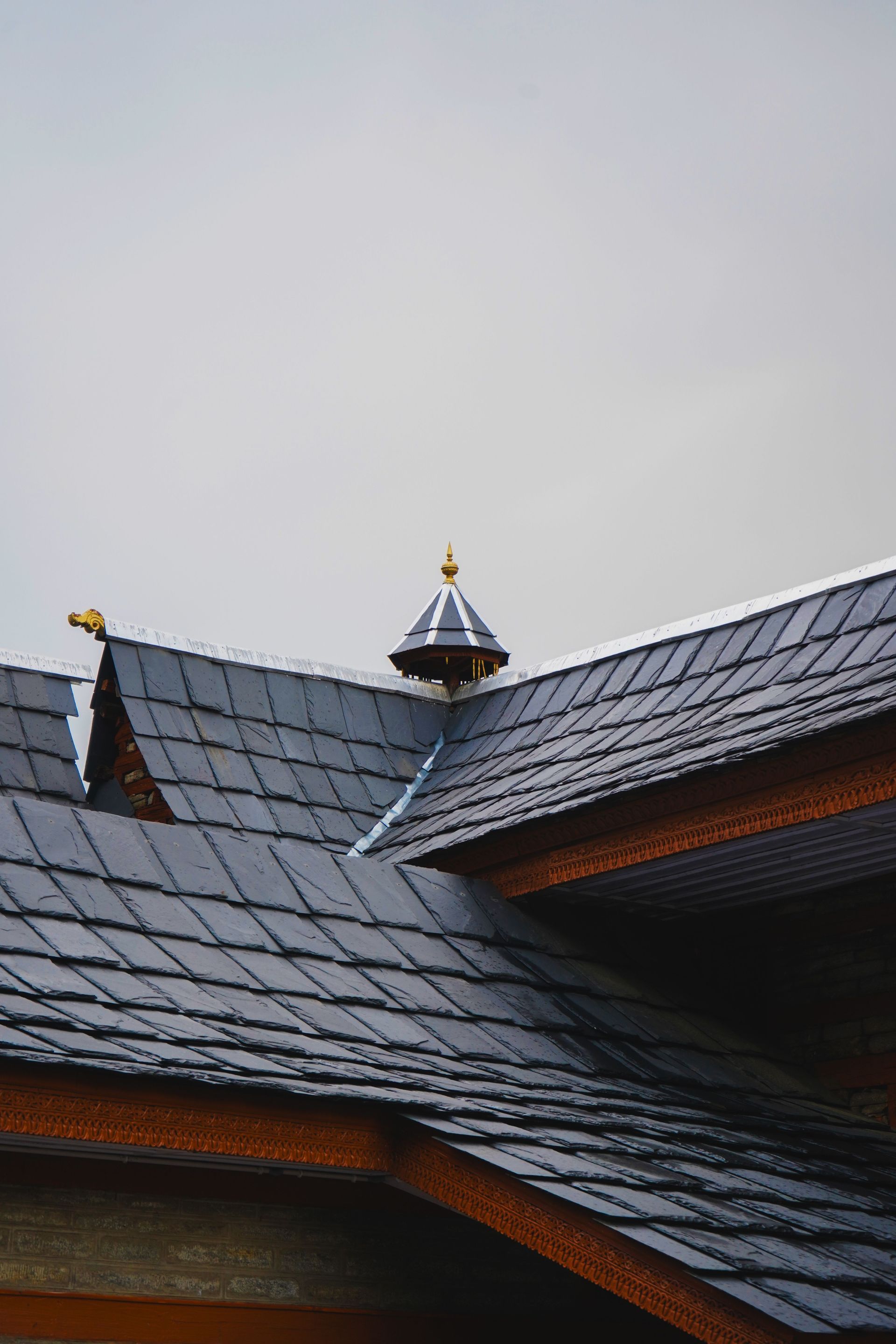 Slate roof with a small decorative tower against a gray sky
