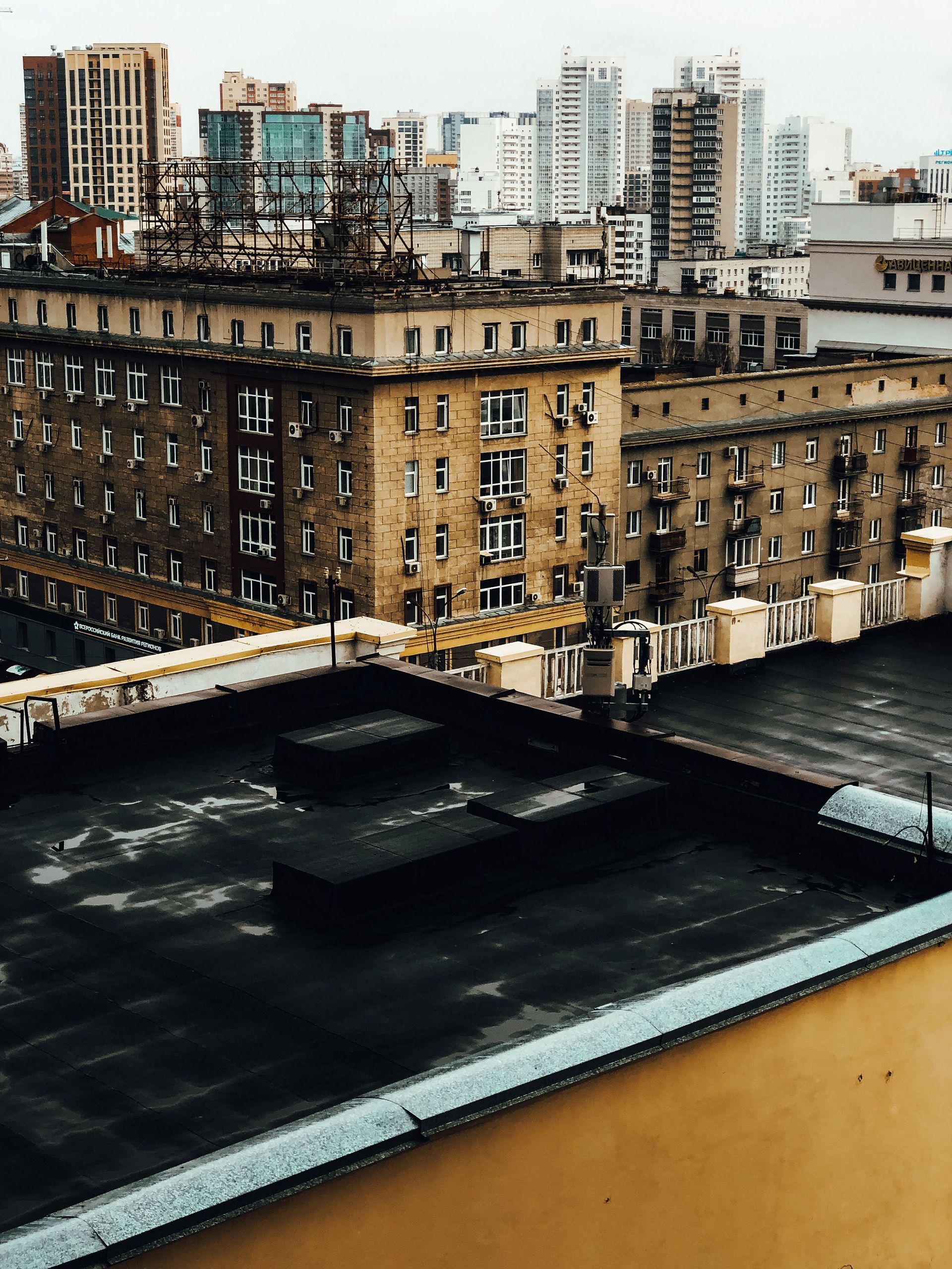 City rooftop view of tan apartment buildings and a dark rooftop under an overcast sky