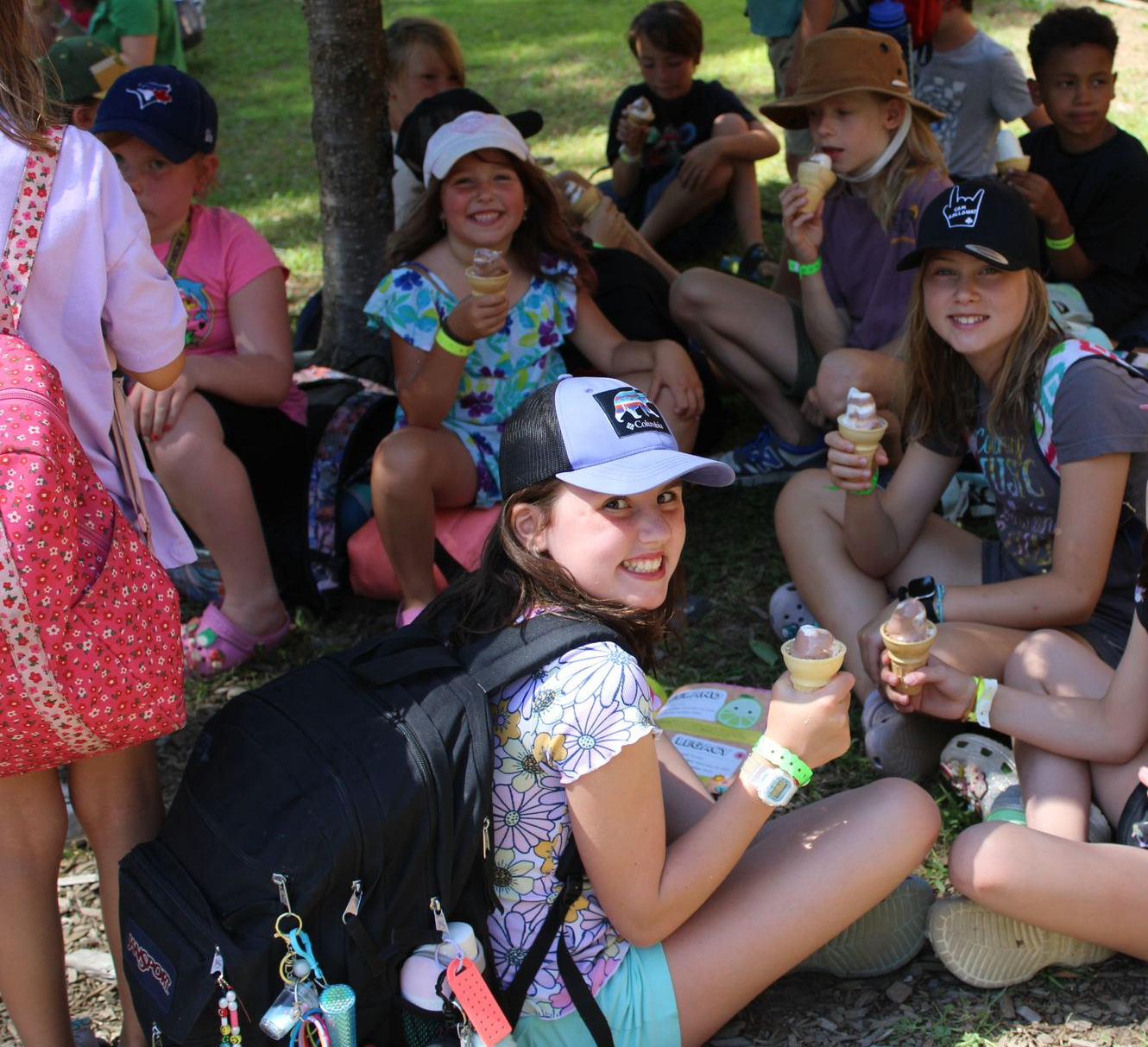 Group of children enjoying ice cream cones, sitting in the shade. Smiles abound.