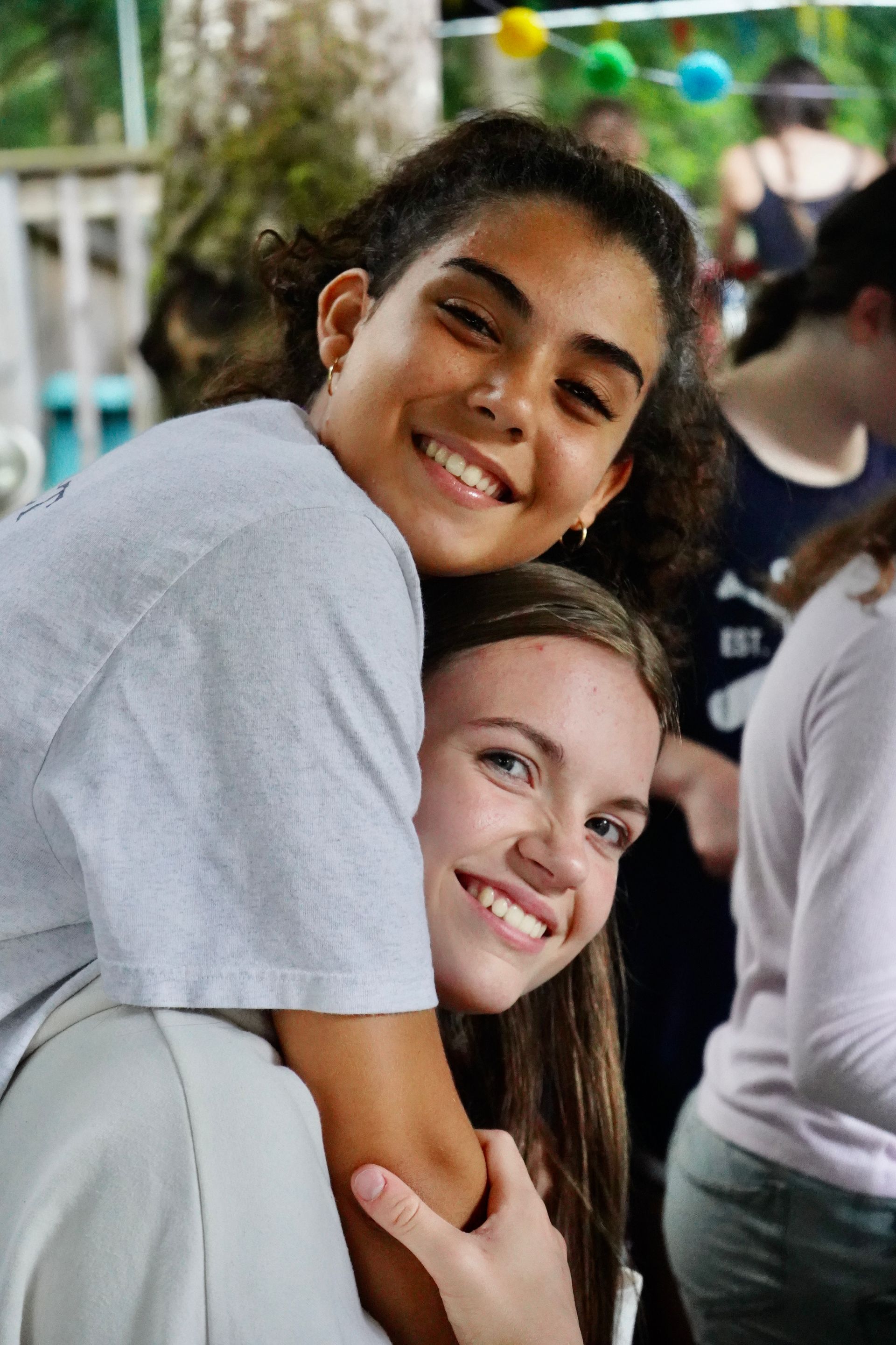 Two young girls are hugging each other and smiling for the camera.