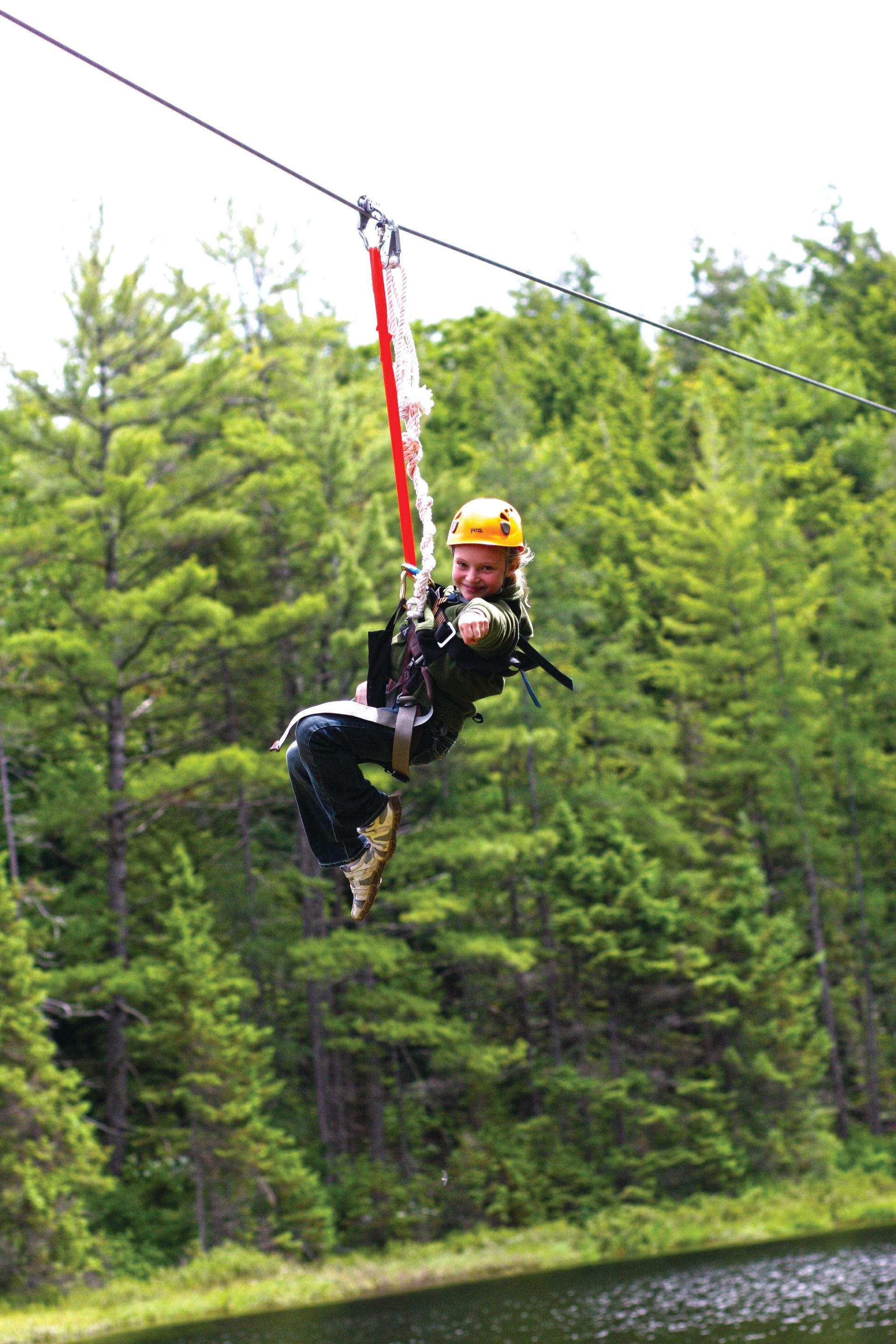 A person is flying through the air on a zip line over a lake.