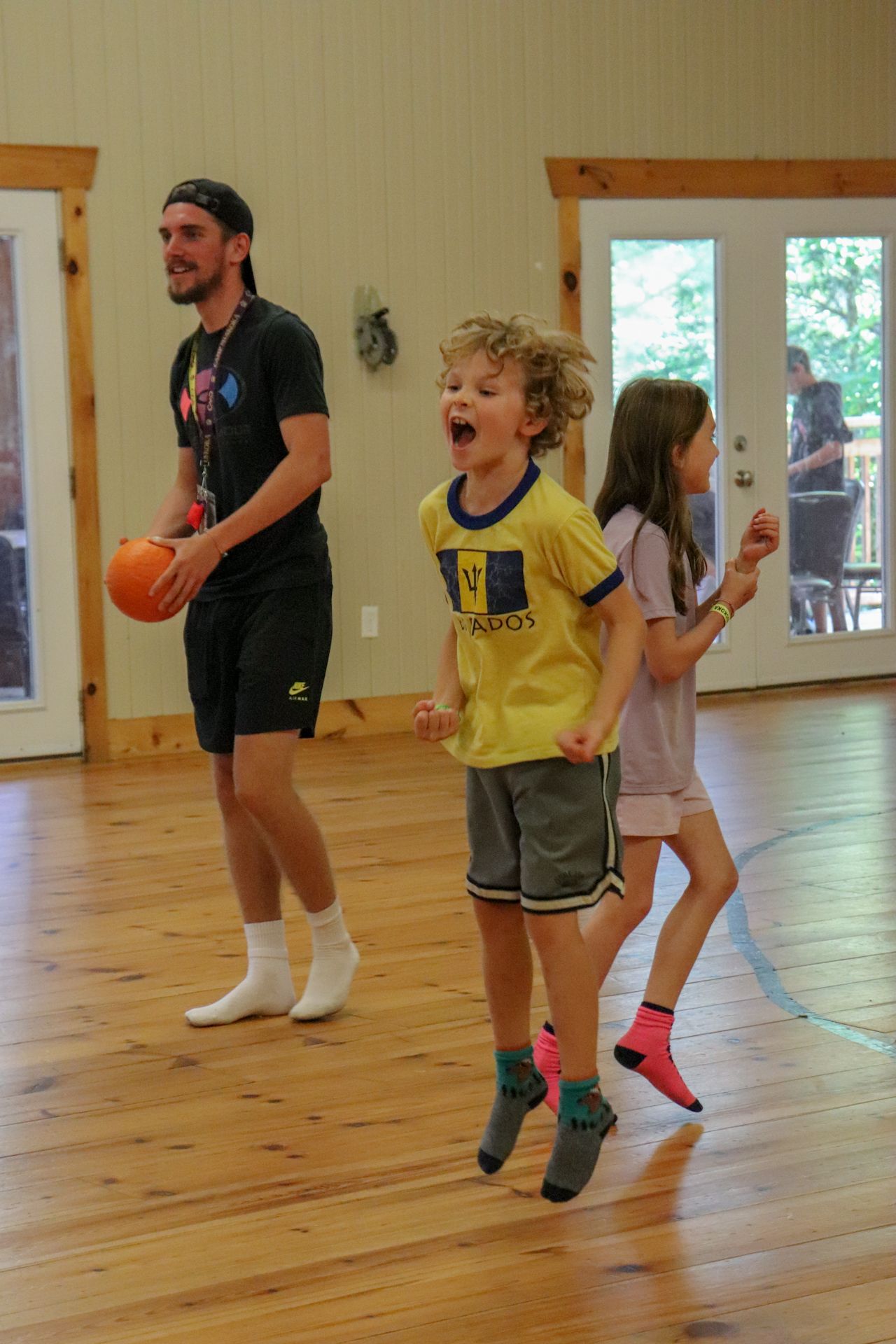 A man and two children are playing with a ball on a wooden floor.