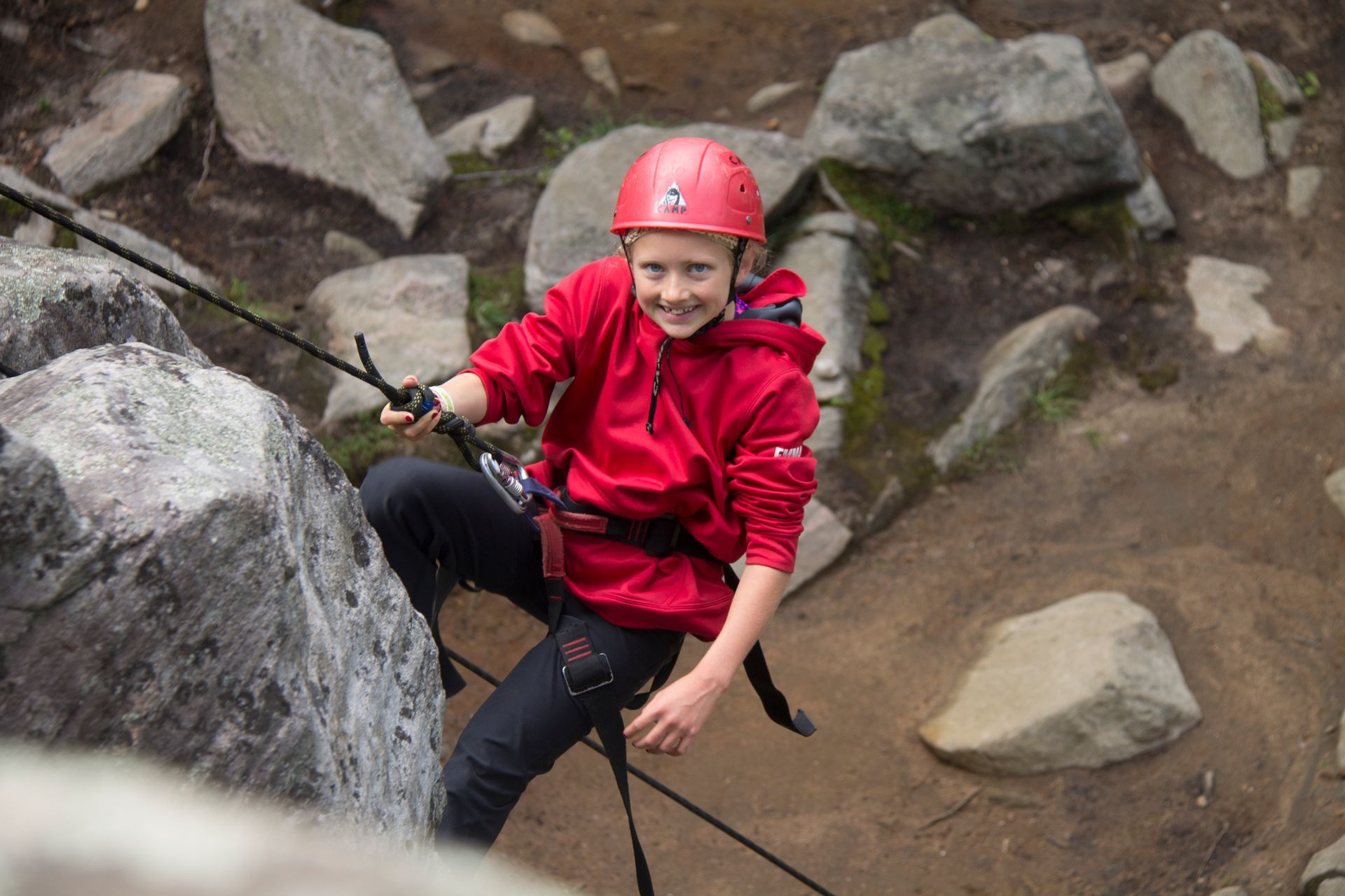Child in red jacket and helmet rock climbing, smiling.