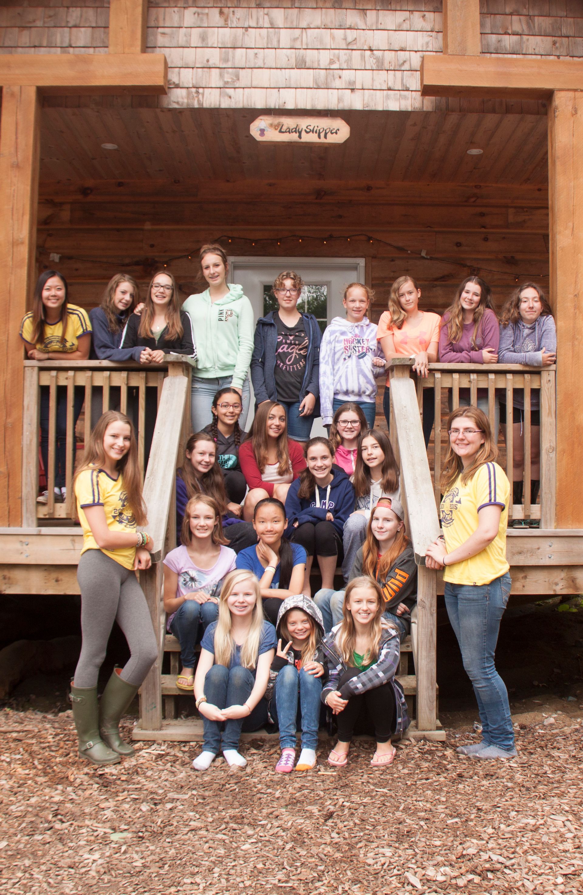 A group of young girls are posing for a picture on the porch of a cabin.