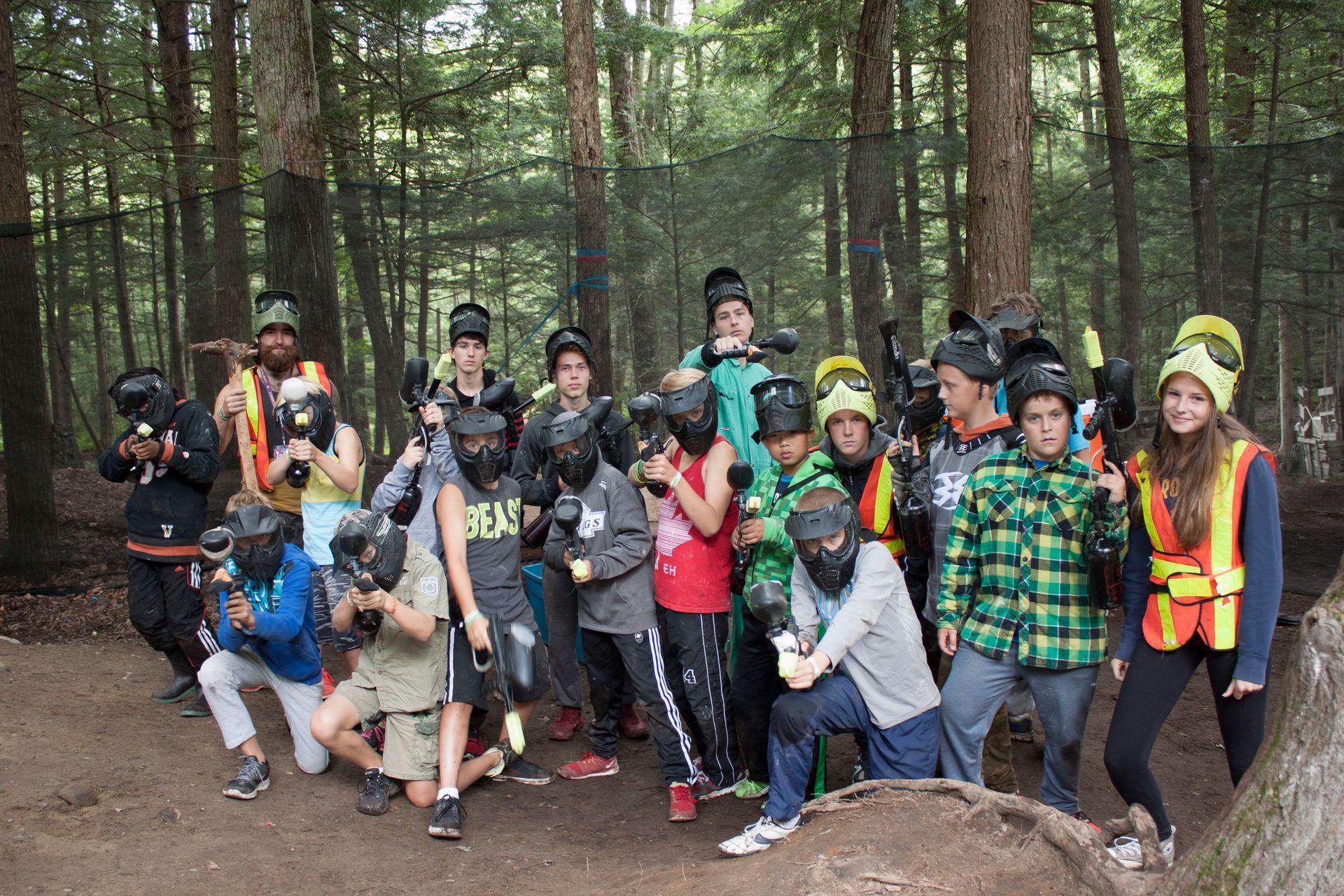 A group of people wearing paintball gear pose with paintball guns in a wooded area.