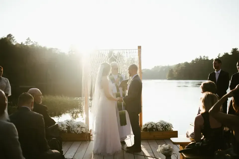 A bride and groom are holding hands during their wedding ceremony on a dock.