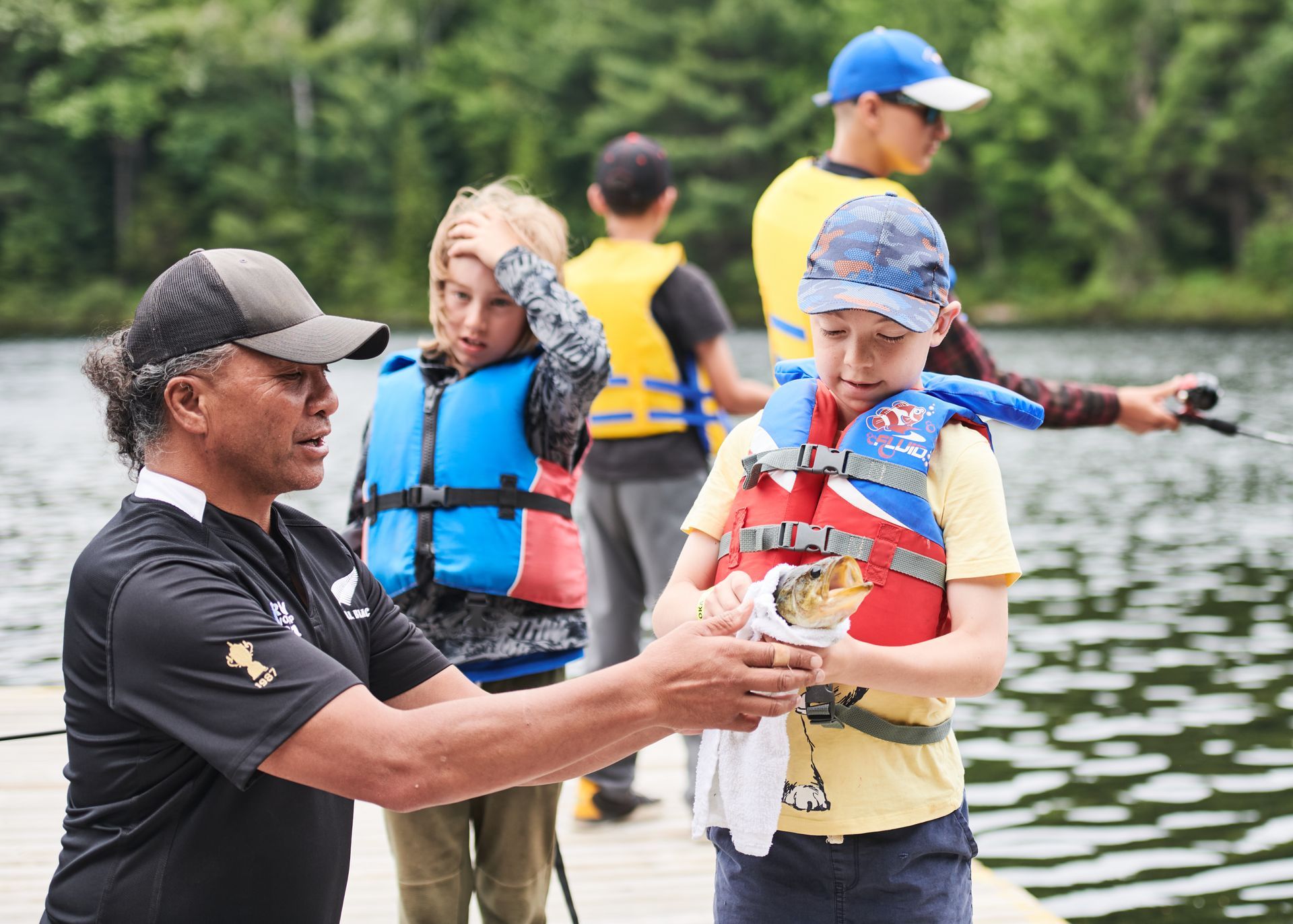 A man is talking to a boy in a life jacket on a dock.
