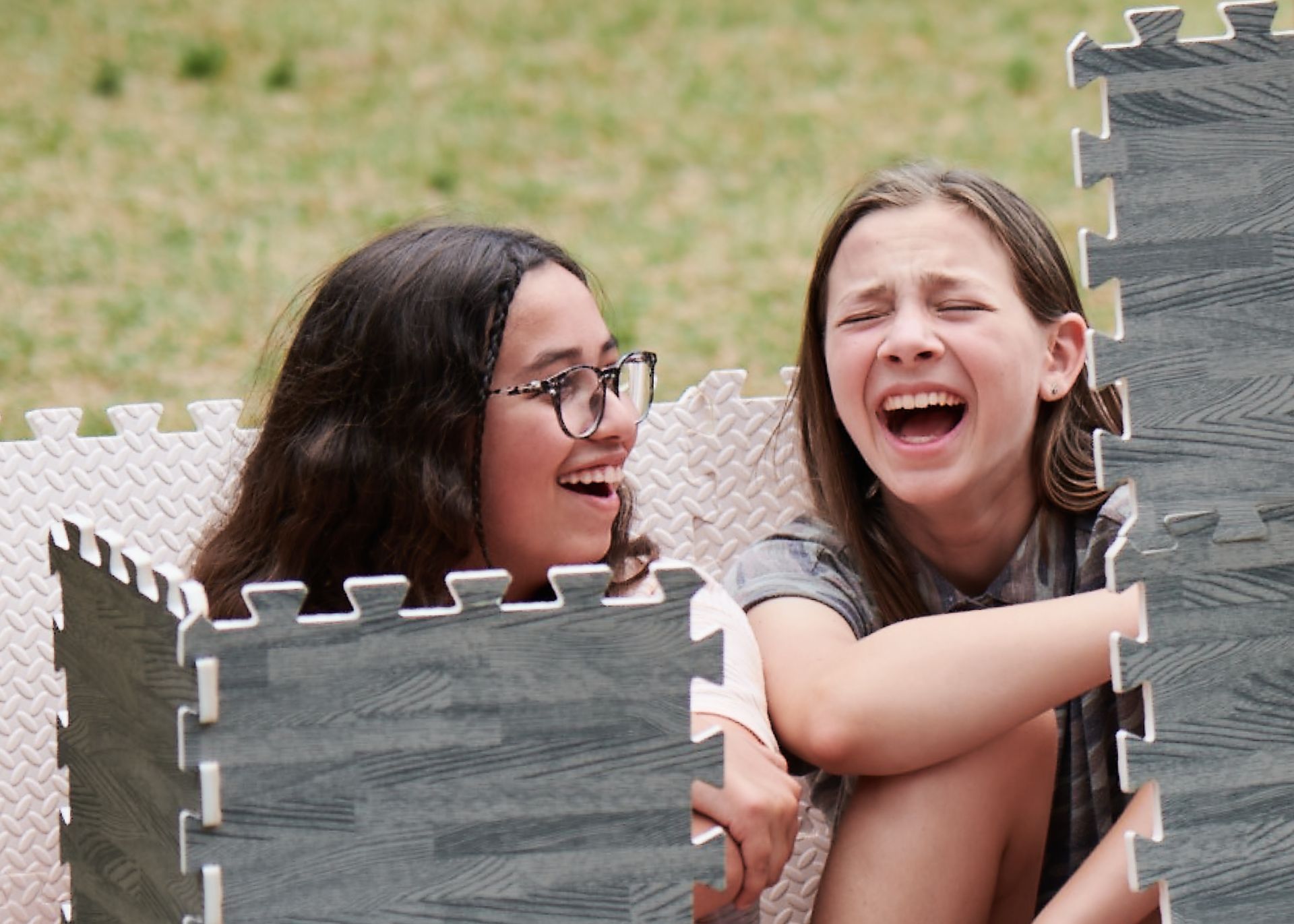 Two young girls are sitting in a puzzle mat and laughing.
