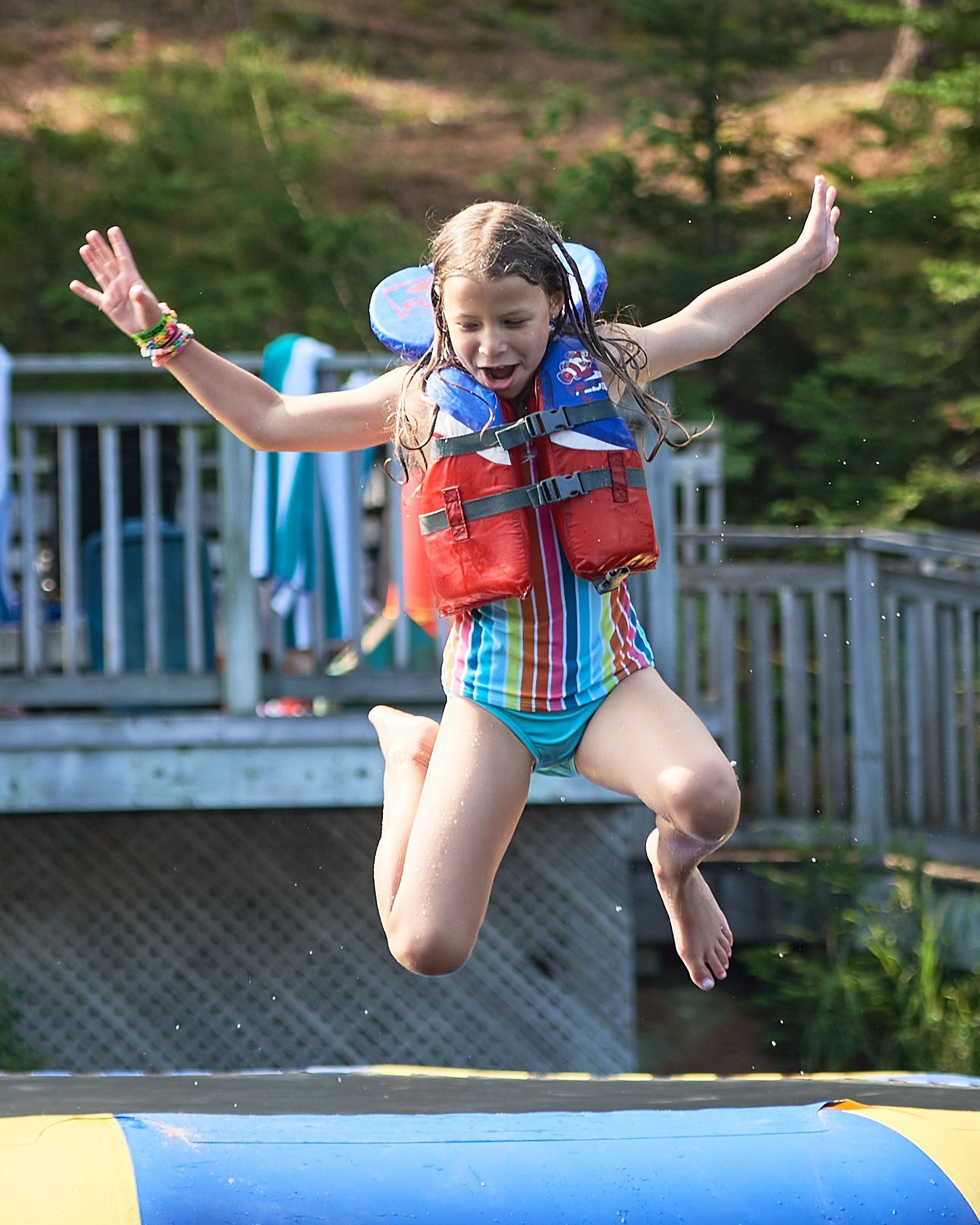A young girl in a life jacket is jumping on a trampoline.